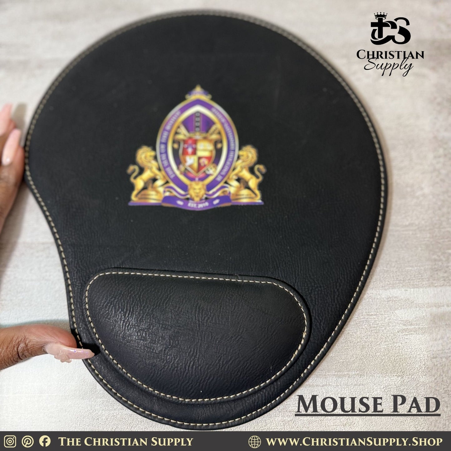 Black mouse pad with a logo on a light gray surface, featuring 'The Christian Supply' branding.